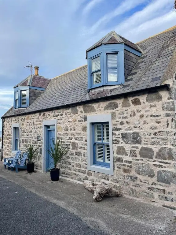 a stone house with blue windows and a bench at Sea Crest - Beachfront Escape with Whisky Snug in Cullen