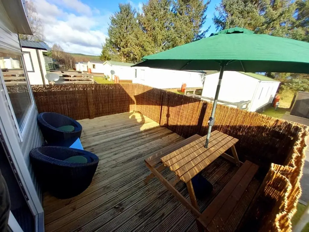 a wooden deck with a green umbrella and a bench at Boat 32 in Boat of Garten