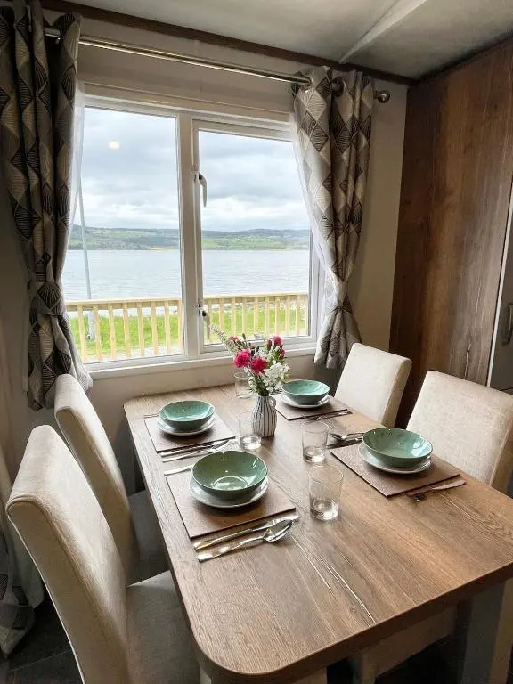 a wooden table with chairs and a large window at Brand New Beautiful Home close to Inverness in North Kessock