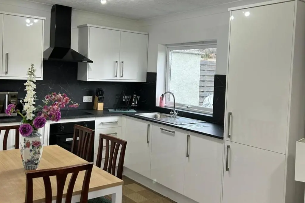 a kitchen with white cabinets and a table with a vase of flowers at Hot tub - Garden - Bbq - Parking - Pets - Sleeps 6 in Strathpeffer