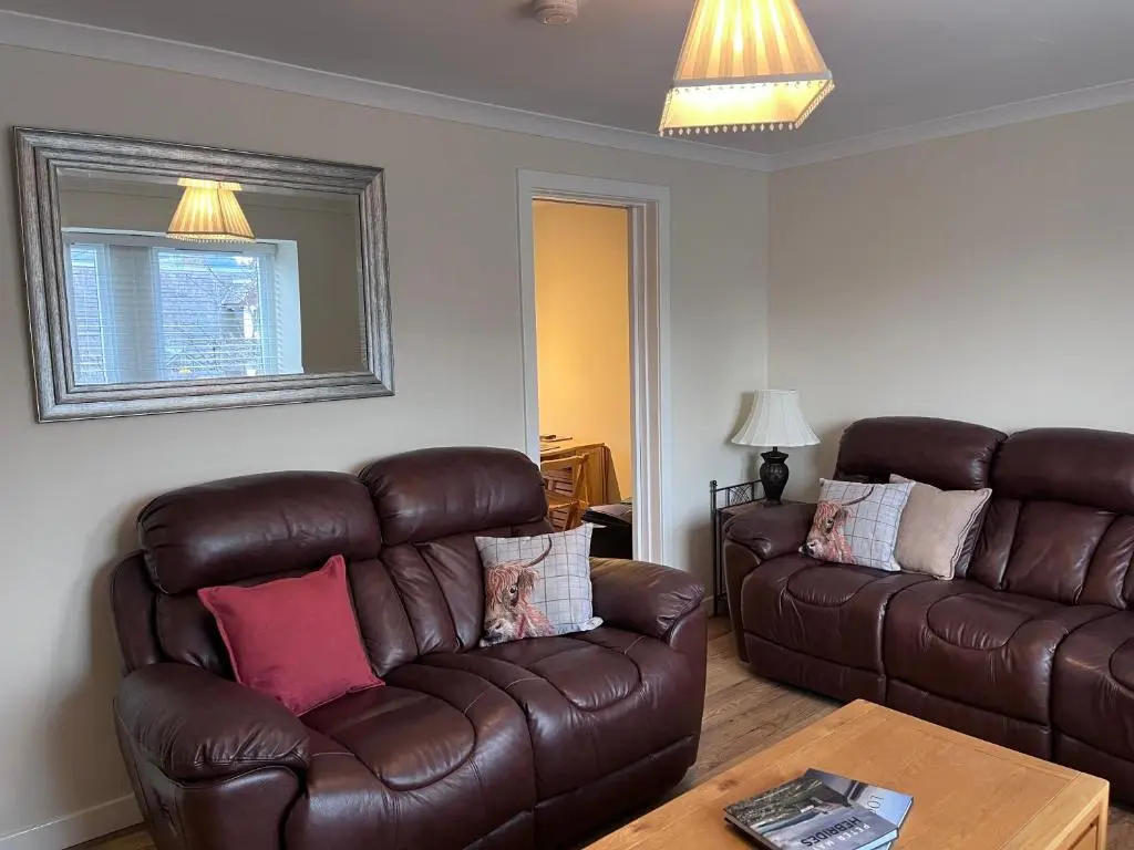 a living room with a leather couch and a table at Millburn Court Apartment in Inverness