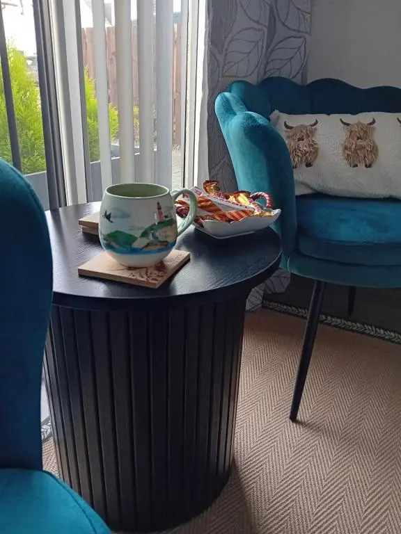 a coffee table with a cup and a blue chair at The Snug on The Brae in Inshes