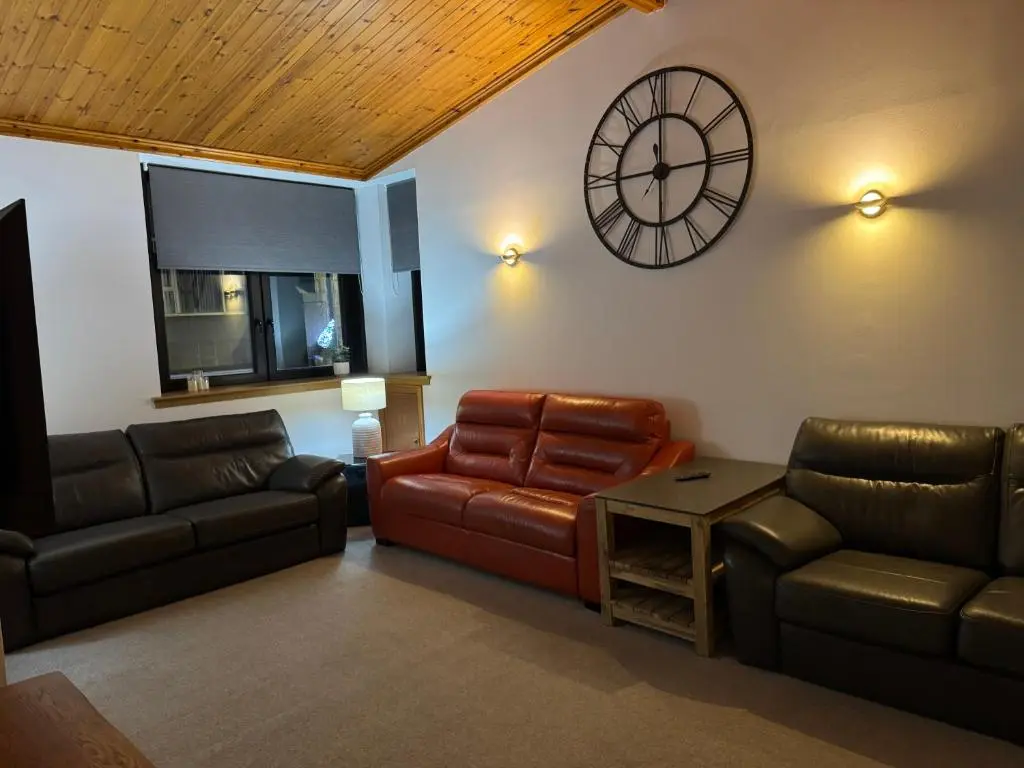 a living room with a couch and a clock on the wall at TSB Accommodation in Turriff