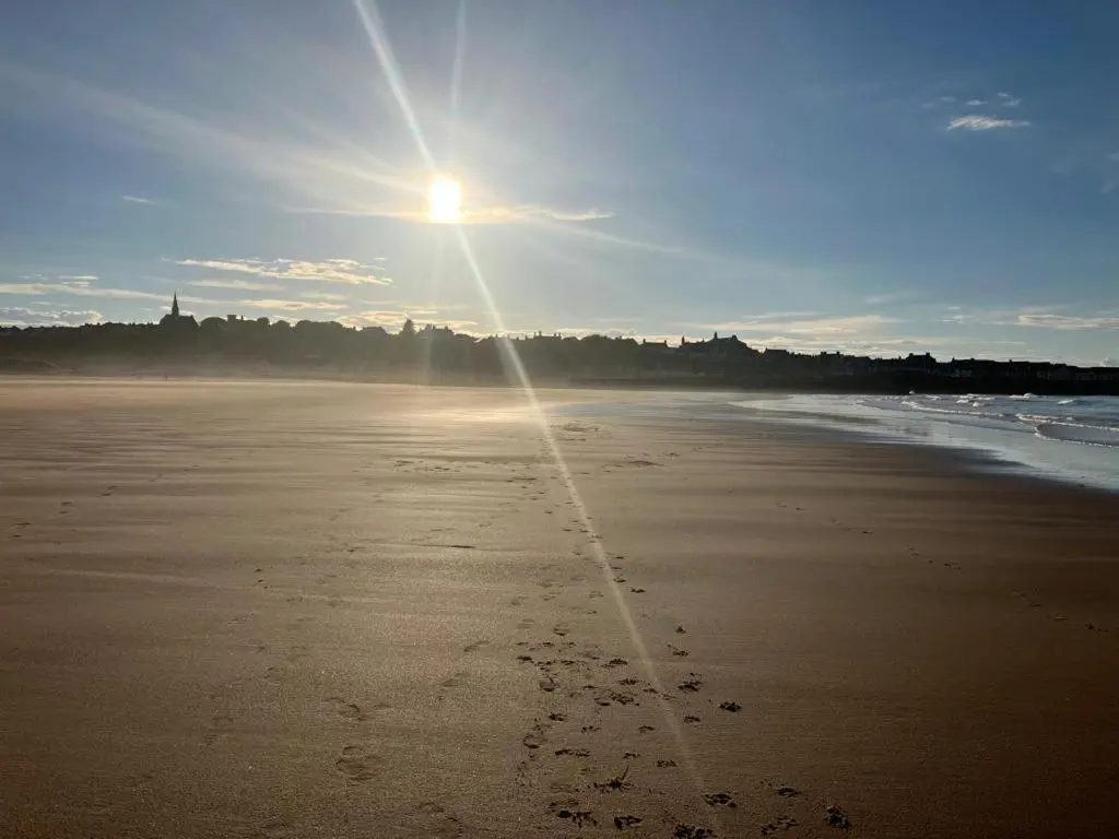 a beach with footprints in the sand and the sun at Moray Coast getaway in Lossiemouth
