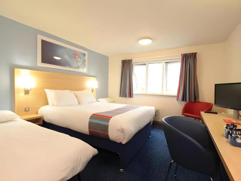 a hotel room with two beds and a desk at Travelodge Inverness Fairways in Inshes