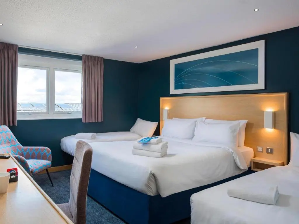 a hotel room with two beds and a desk at Travelodge Aberdeen Bucksburn in Aberdeen