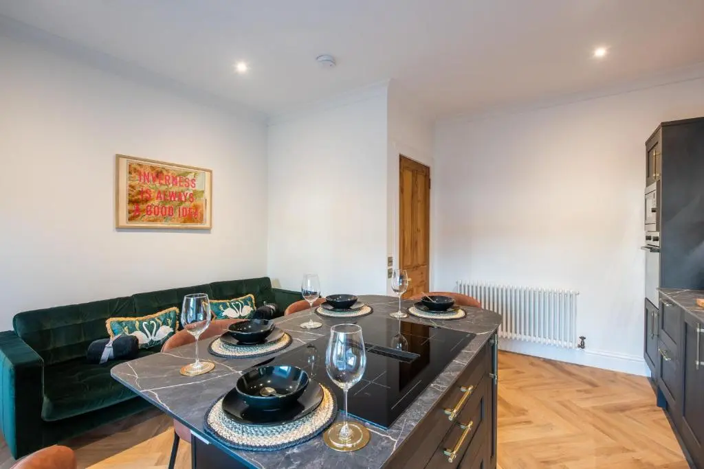 a living room with a green couch and a table with wine glasses at Luxury New Inverness Apartment in a Prime Location in Inverness