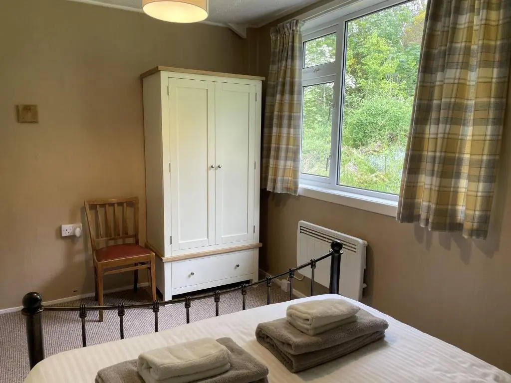 a bedroom with a bed with a cabinet and a chair at Crianlarich Cottage in Fort Augustus