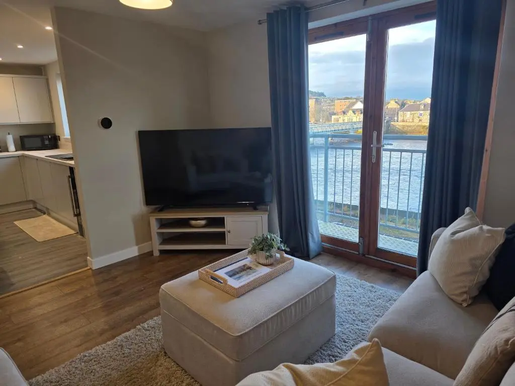 a living room with a television and a large window at Riverside View in Inverness