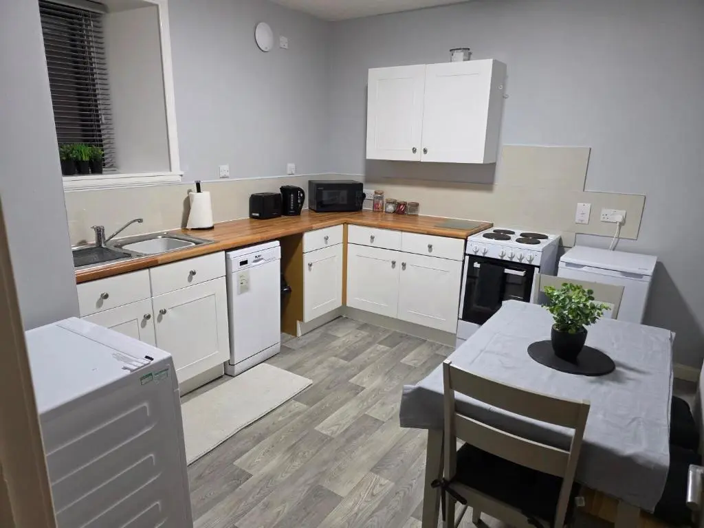 a kitchen with white cabinets and a table and a sink at 14 Harbour View in Wick