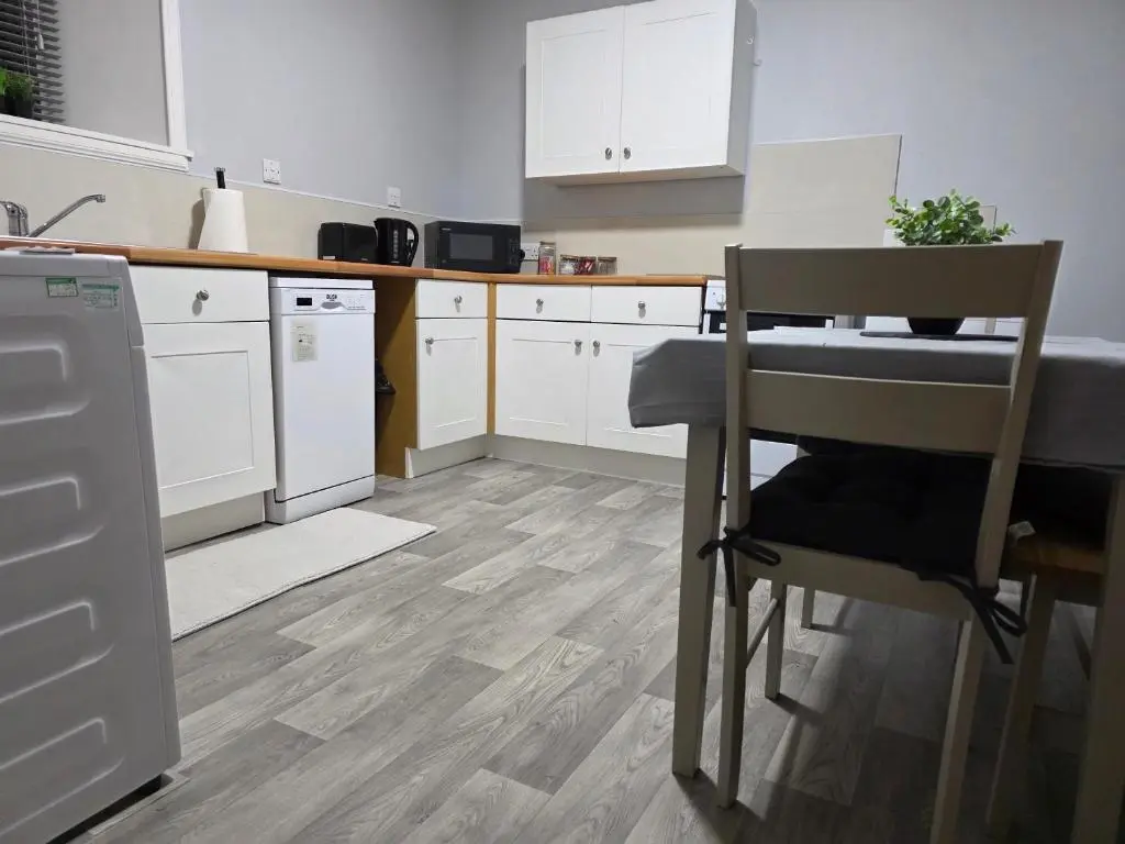 a kitchen with white cabinets and a table and a chair at 14 Harbour View in Wick