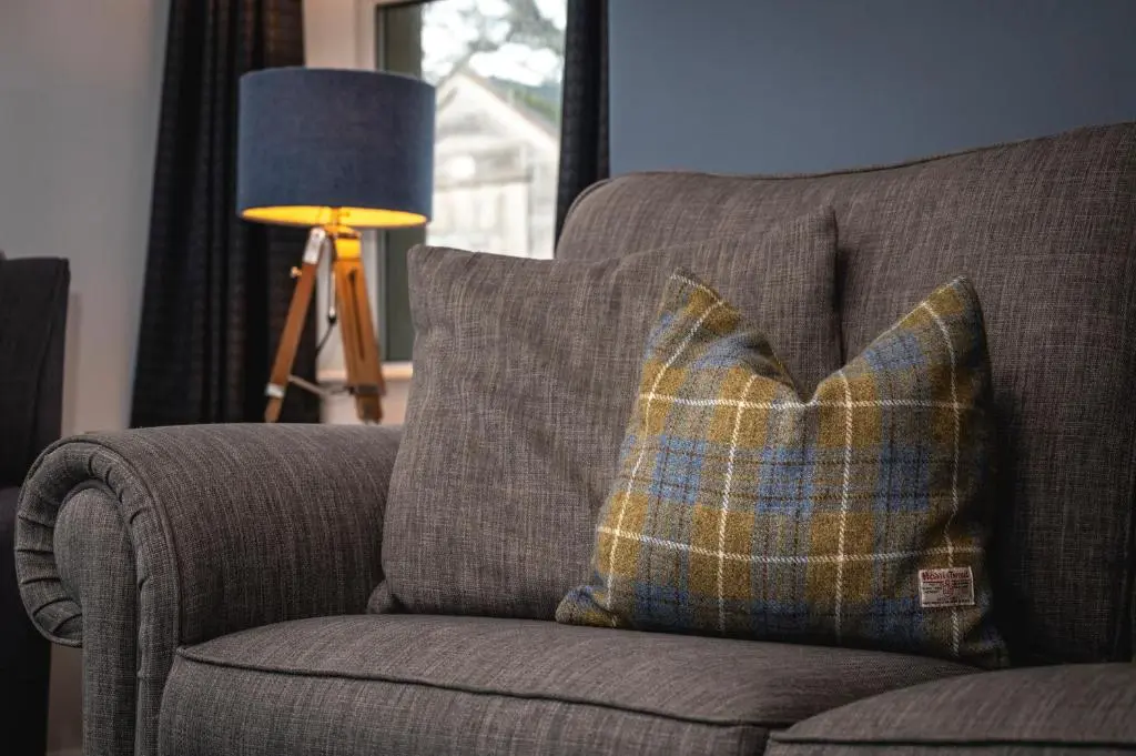 a plaid pillow on a couch next to a lamp at Burnside, Dornoch in Dornoch