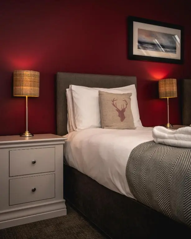 a bedroom with a bed with red walls and two lamps at Burnside, Dornoch in Dornoch