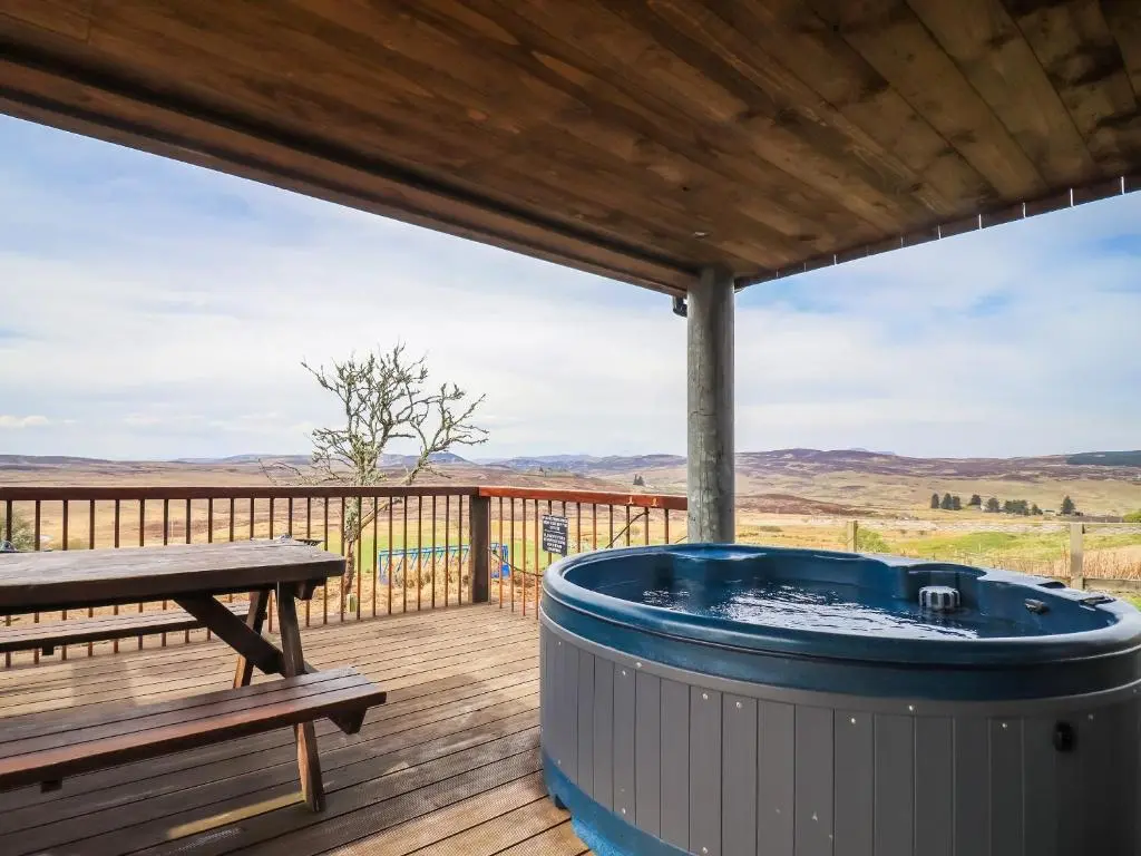 a hot tub on a deck with a bench at Kestrel Cottage in Rogart