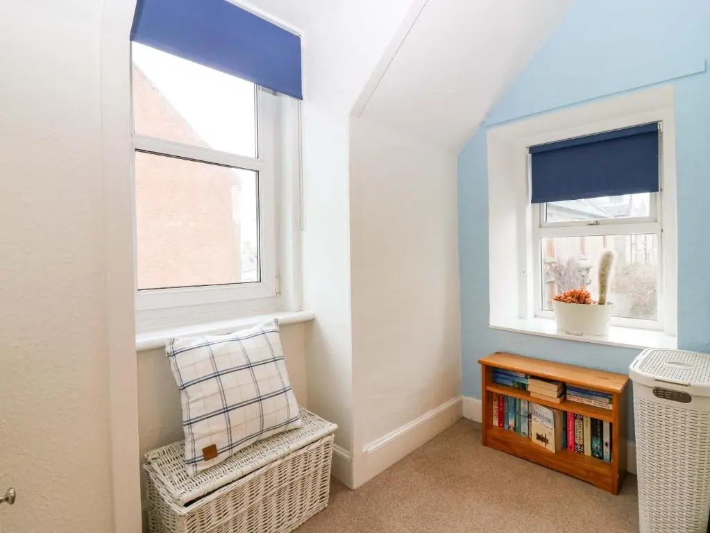 a room with a book shelf and two windows at Rose Cottage in Nairn