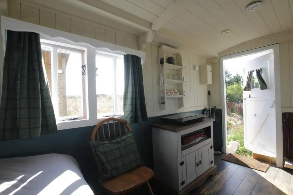 a bedroom with a bed and two windows and a chair at The Rumster Hut in Lybster