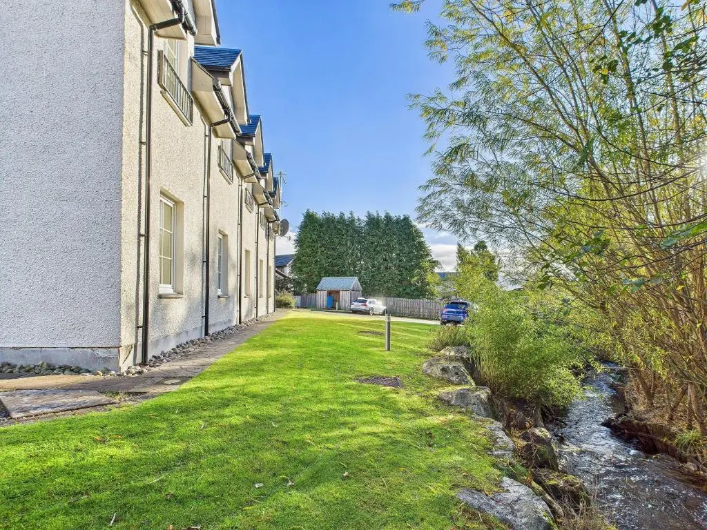 a house with a grass yard next to a building at The Steadings Aviemore Premium Highland Apartment Near Cairngorms & Town Centre in Aviemore