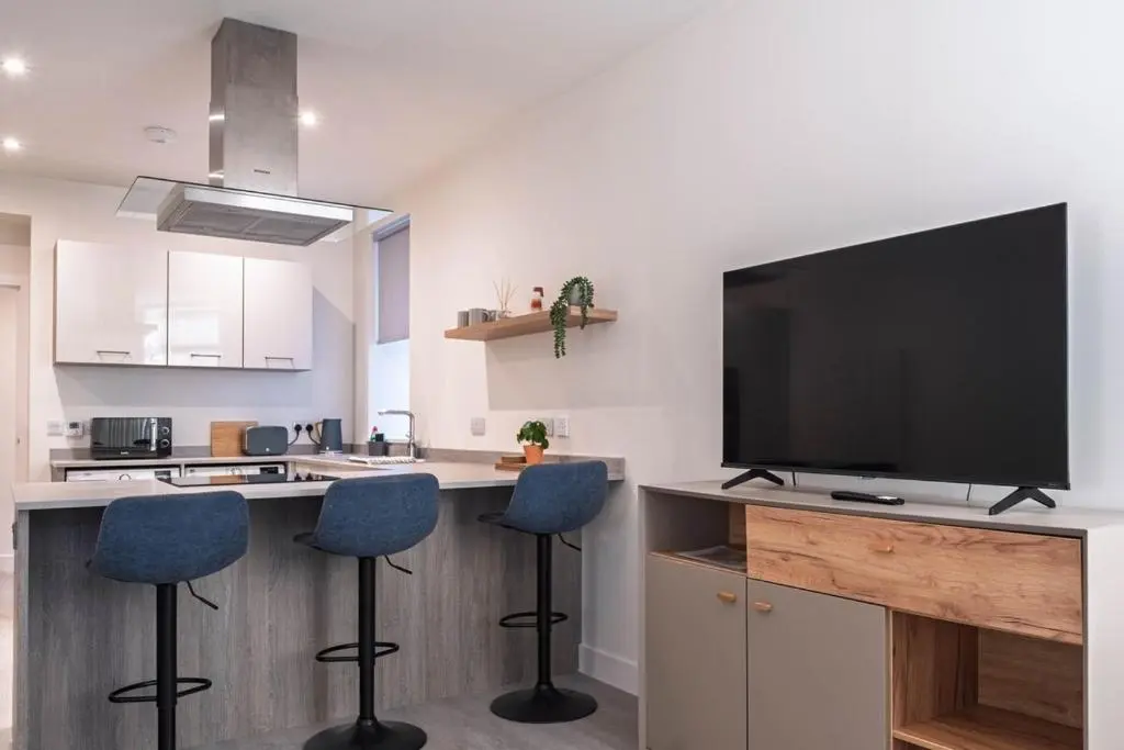 a kitchen with a bar with two stools and a flat screen tv at Modern Central Apartment Huntly in Huntly