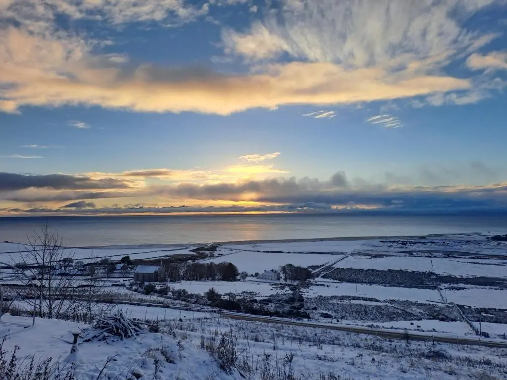 a view of a snowy field with the ocean in the background at Lothmore Lookout - Sunrise in Kilmote