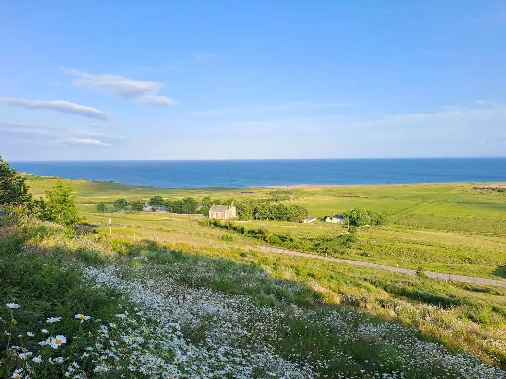 a view of a field with the ocean in the background at Lothmore Lookout - Sunrise in Kilmote