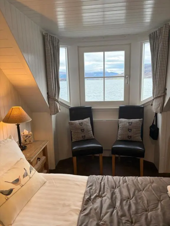 a bedroom with two chairs and a bed and two windows at Waterside House B&B in Ullapool