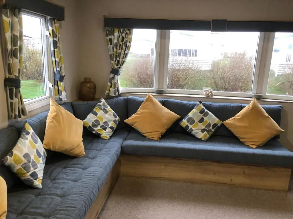 a blue couch with yellow pillows sitting in front of windows at Dunes Escape in Lossiemouth