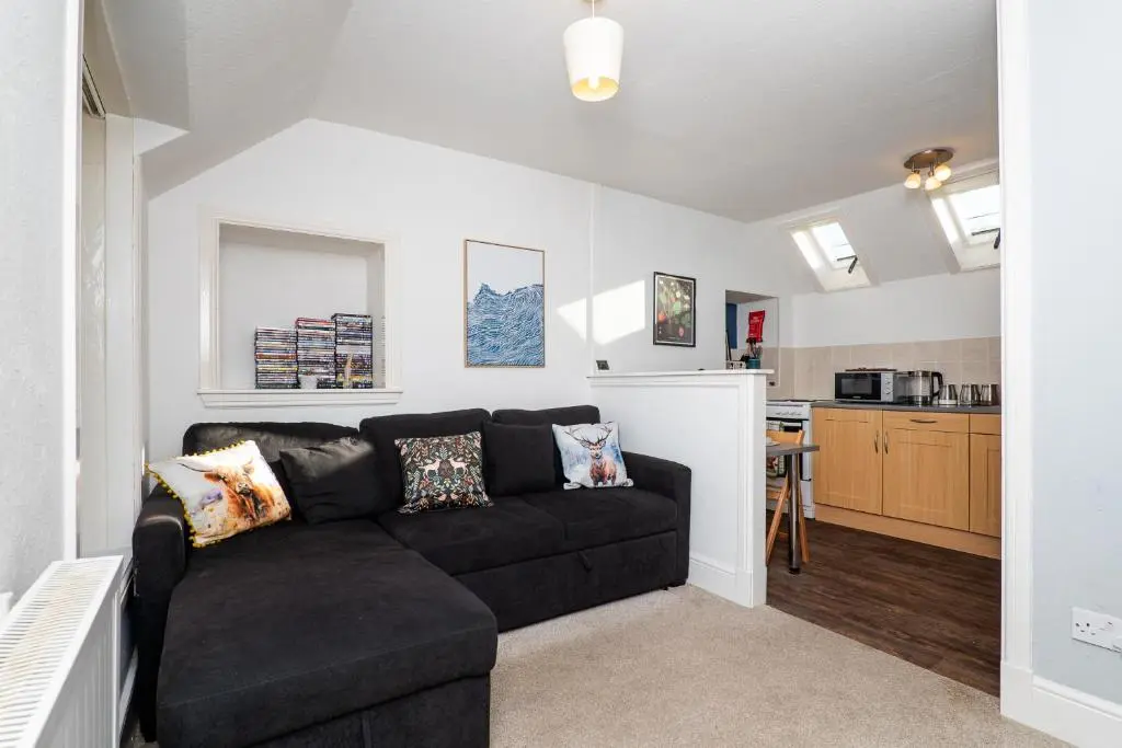 a living room with a black couch and a kitchen at Charming 1-Bed Coastal Cottage by Holiday Homes in Portgordon