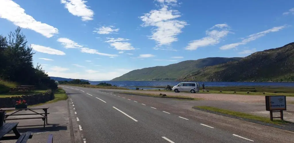 a road with a van parked on the side of a lake at The Dundonnell Hotel in Dundonnell