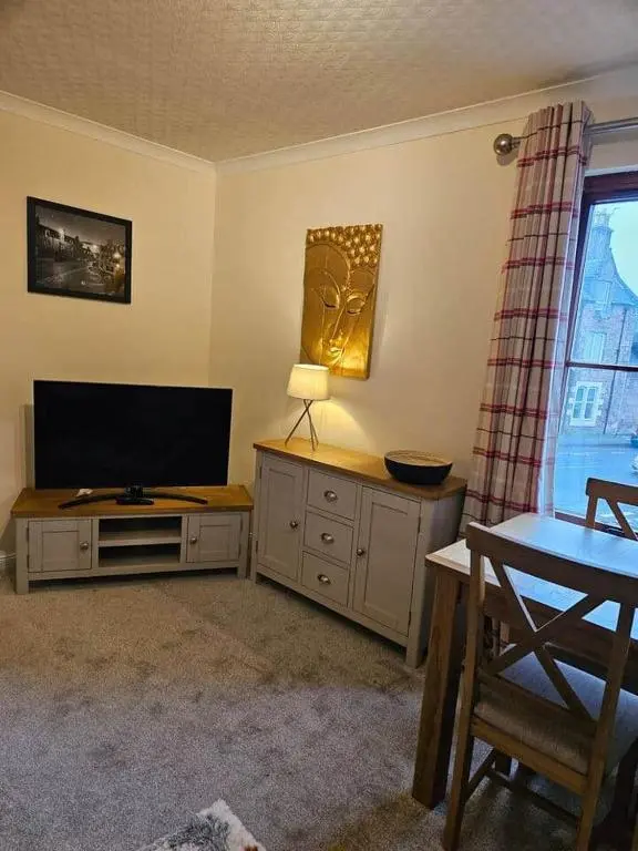 a living room with a flat screen tv and a table at 5 Ardross Court, 20 Ardross St. Inverness IV3 5NH in Inverness