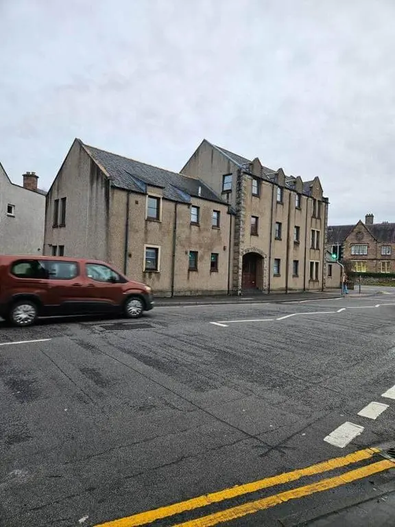 a red car driving down a street next to a building at 5 Ardross Court, 20 Ardross St. Inverness IV3 5NH in Inverness