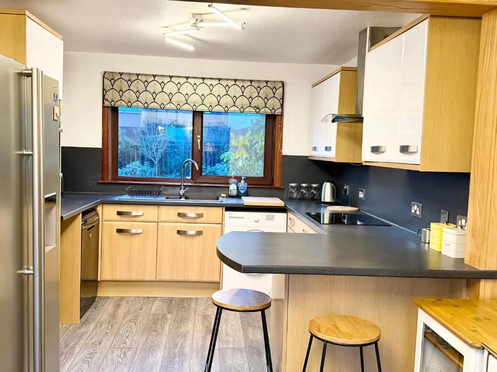 a kitchen with wooden cabinets and a sink and two stools at Mamore House Inverness in Dalneigh