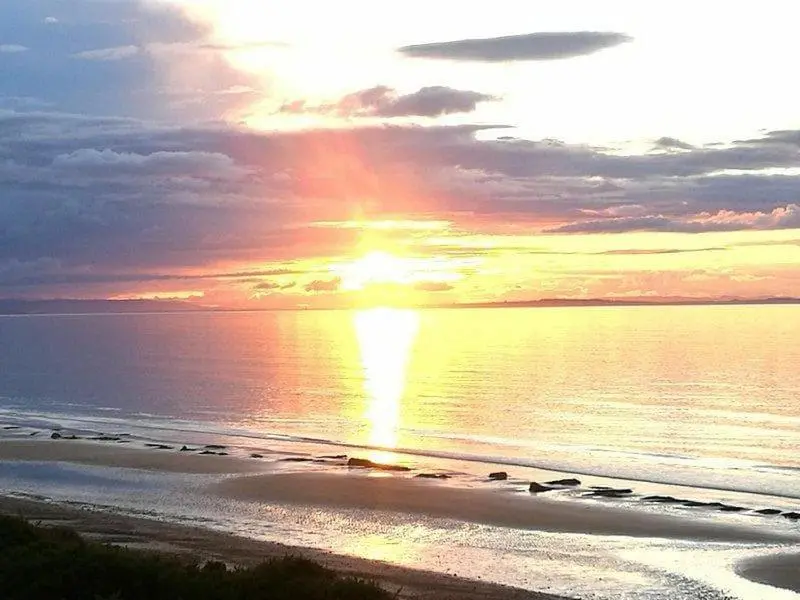 a sunset over a beach with birds on the water at Harbour Haven in Burghead