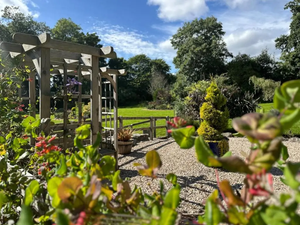 a garden with a wooden pergola and flowers at Drummuie House in Golspie