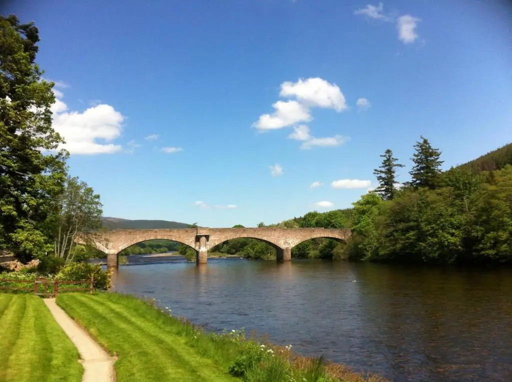 a bridge over a river with green grass and trees at Alexandra Hotel in Ballater