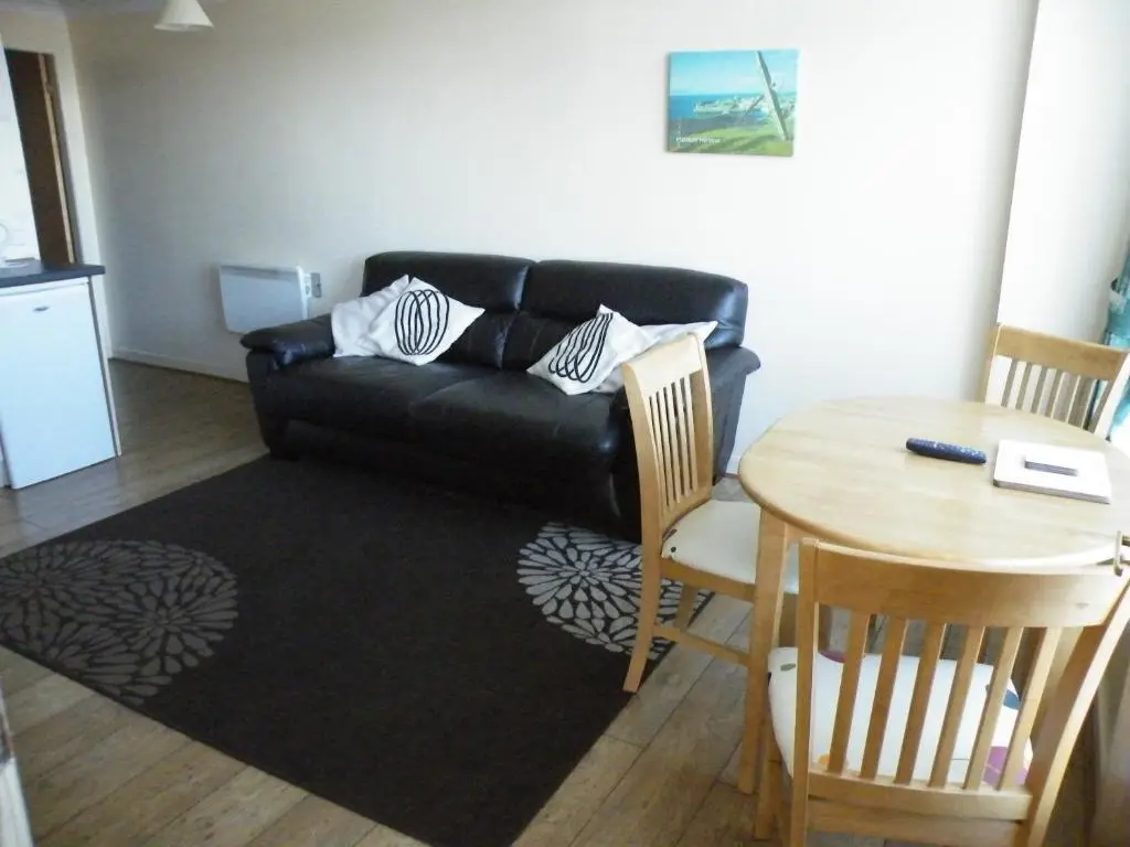 a living room with a black leather couch and a table at Coasters Holiday Flats in Macduff