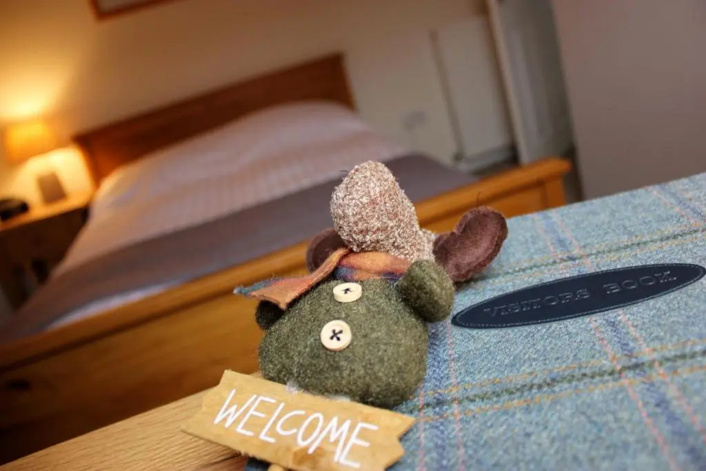 a stuffed animal sitting on a bed with a welcome sign at The Loft, Inverness in Inverness