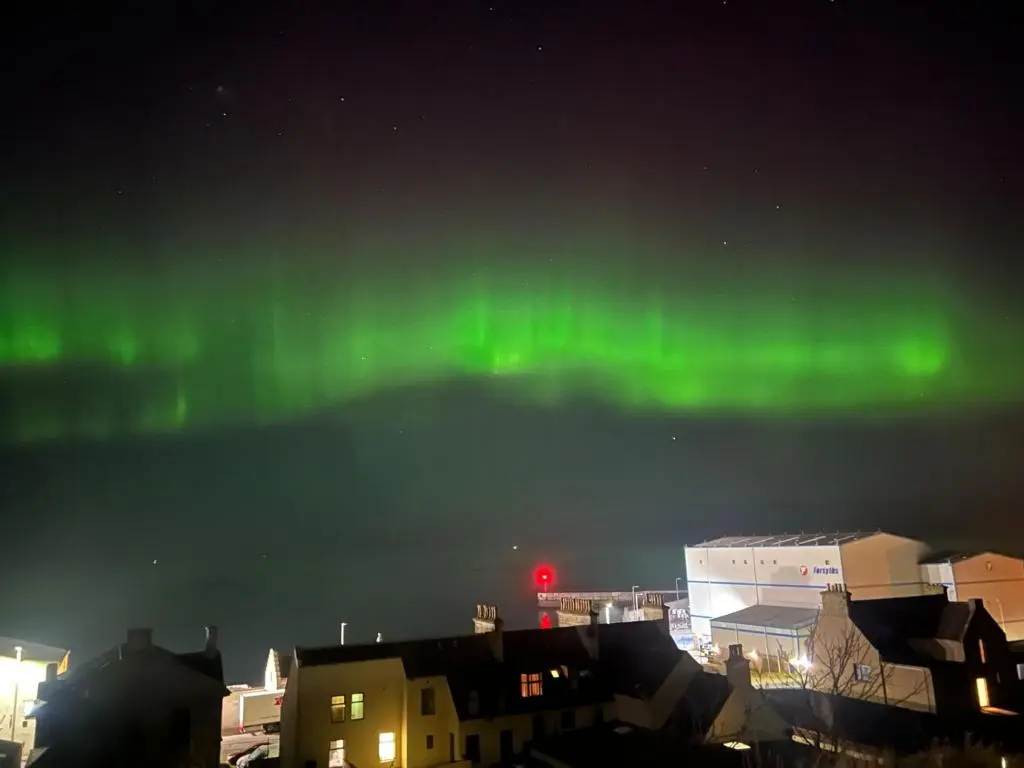 an aurora in the sky over a city with buildings at Kintrae B&B in Buckie