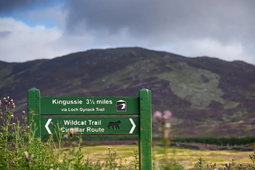 a green sign in front of a mountain at The Balavil Hotel Newtonmore - Restaurant, Bars & Swimming Pool in Newtonmore