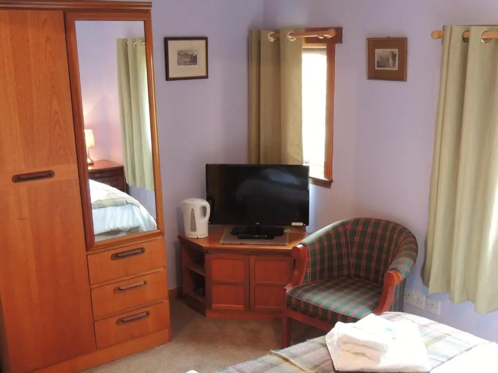 a bedroom with a bed and a tv and a chair at Invicta House B&B in Golspie