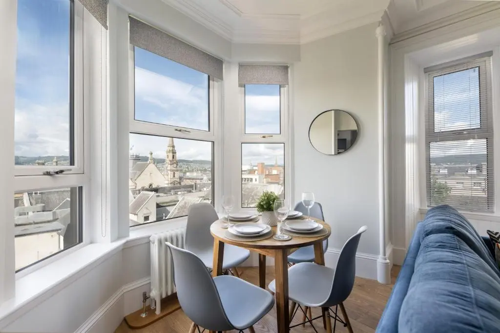 a living room with a table and chairs and windows at Glenmoriston Town House Apartments in Inverness