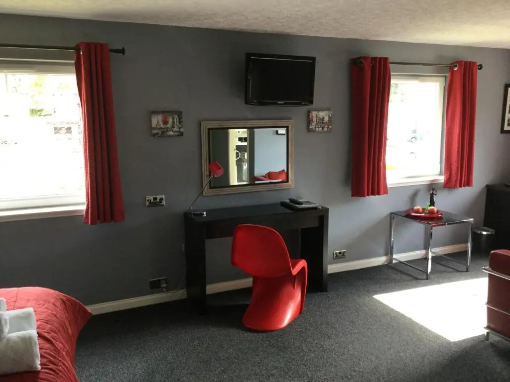 a bedroom with a red chair and a mirror at Dionard Guest House in Inverness