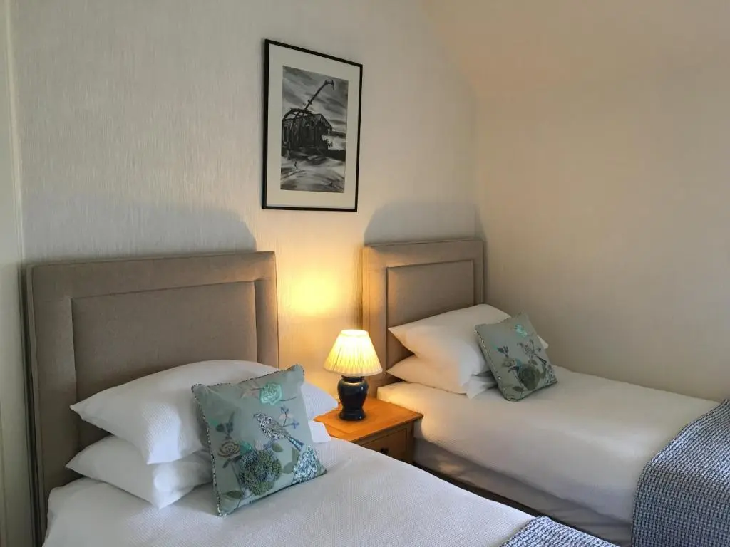 two beds in a room with a lamp on a table at Ronas House in Inverness