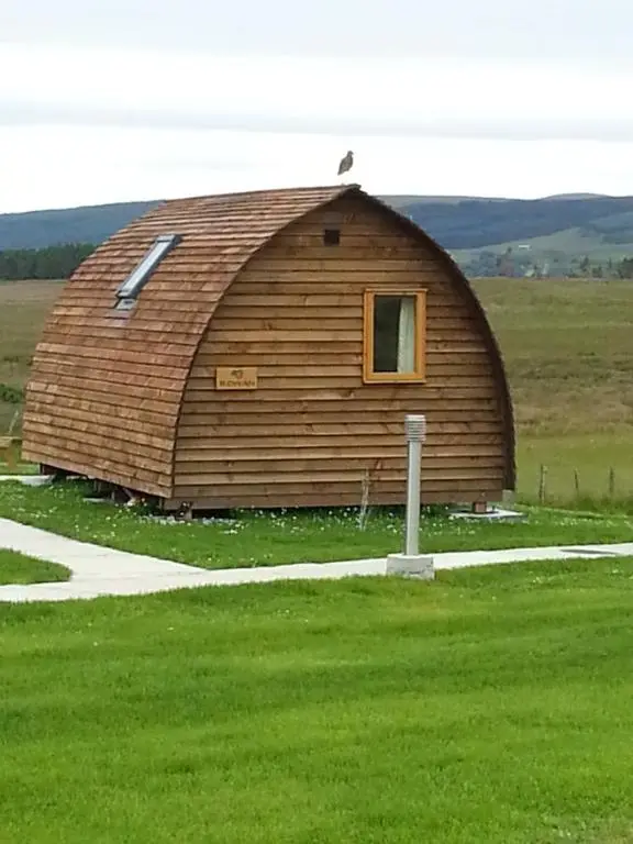 a large wooden barn in the middle of a field at Loch Shin Glamping Pods in Lairg
