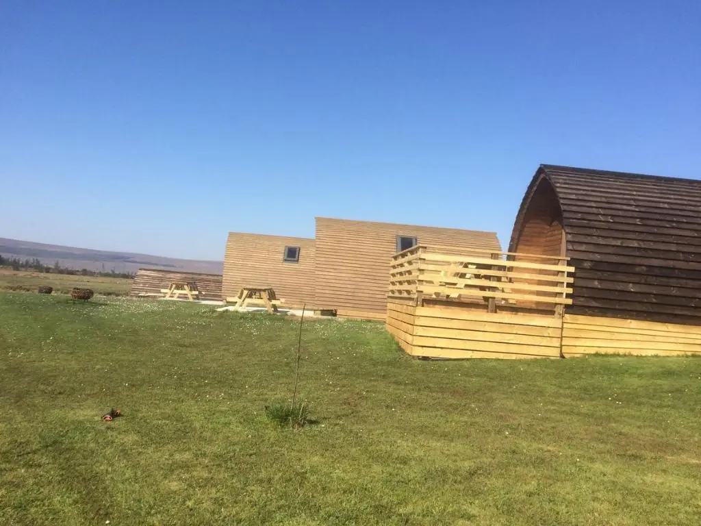 a house in a field next to a building at Loch Shin Glamping Pods in Lairg