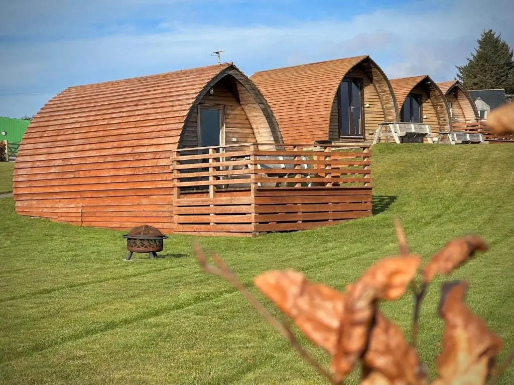 a large wooden building in a field with a yard at Loch Shin Glamping Pods in Lairg