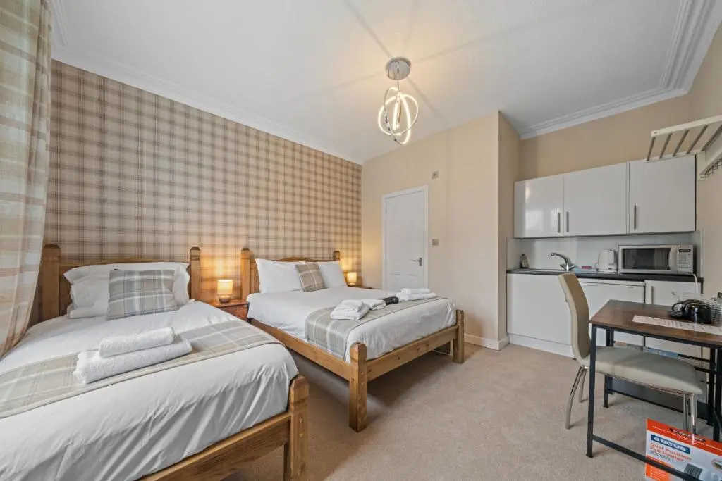 a bedroom with two beds and a table and a kitchen at mySTAYINN Strathblane House in Inverness