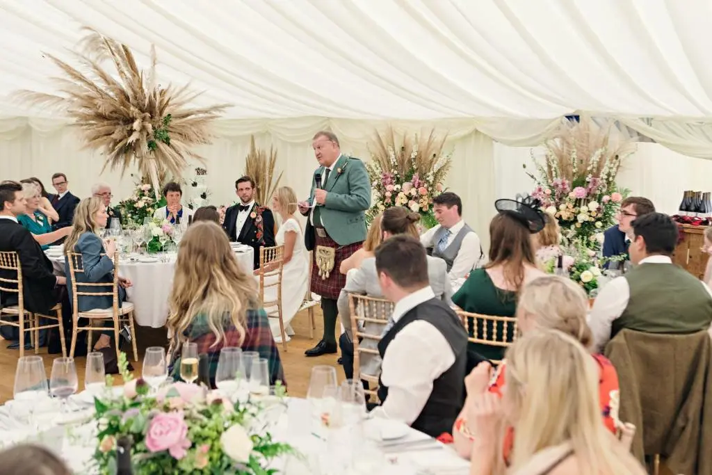 a man giving a speech at a wedding reception in a white tent at Dalvey House in Forres