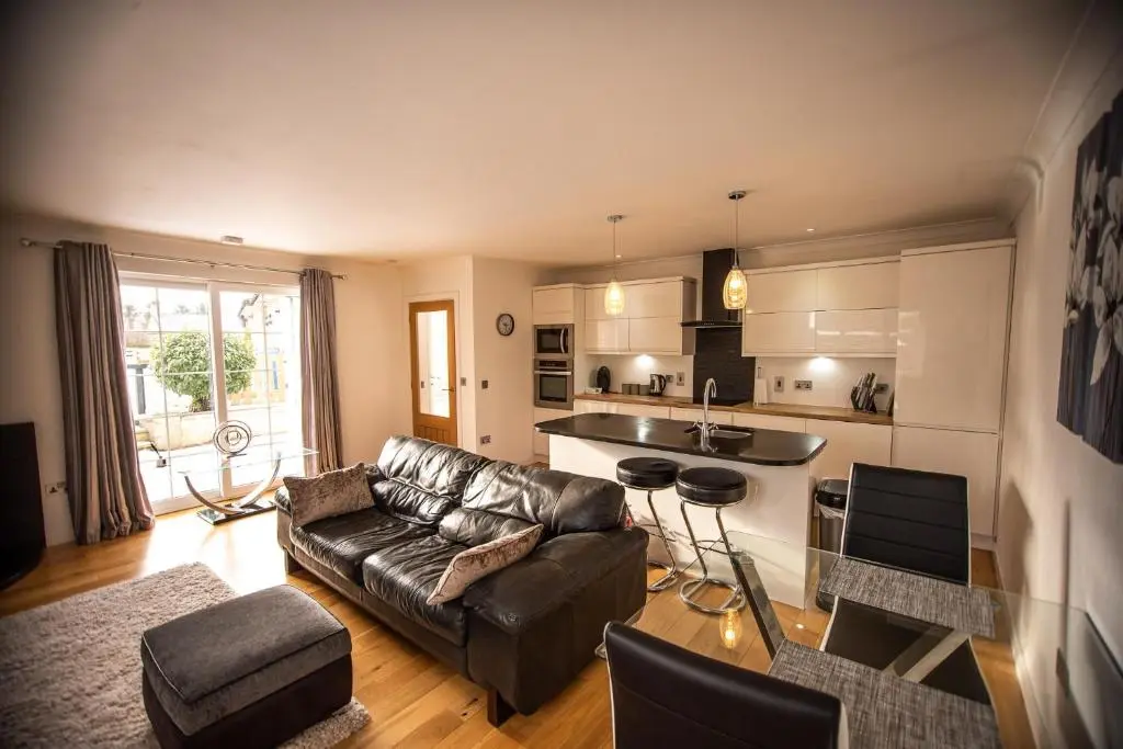 a living room with a leather couch and a kitchen at Langley Cottage with patio, spacious rooms - part of Langley Serviced Apartments several properties in Wick in Wick