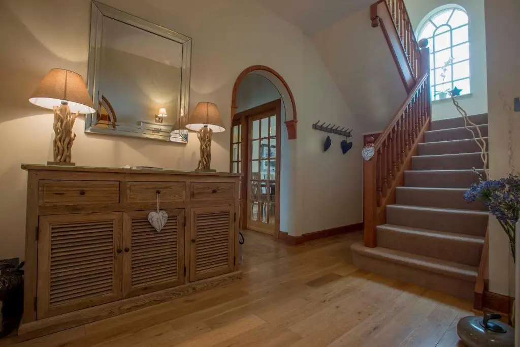 a hallway with a staircase and a dresser with a mirror at Sea View Lodge in Nairn