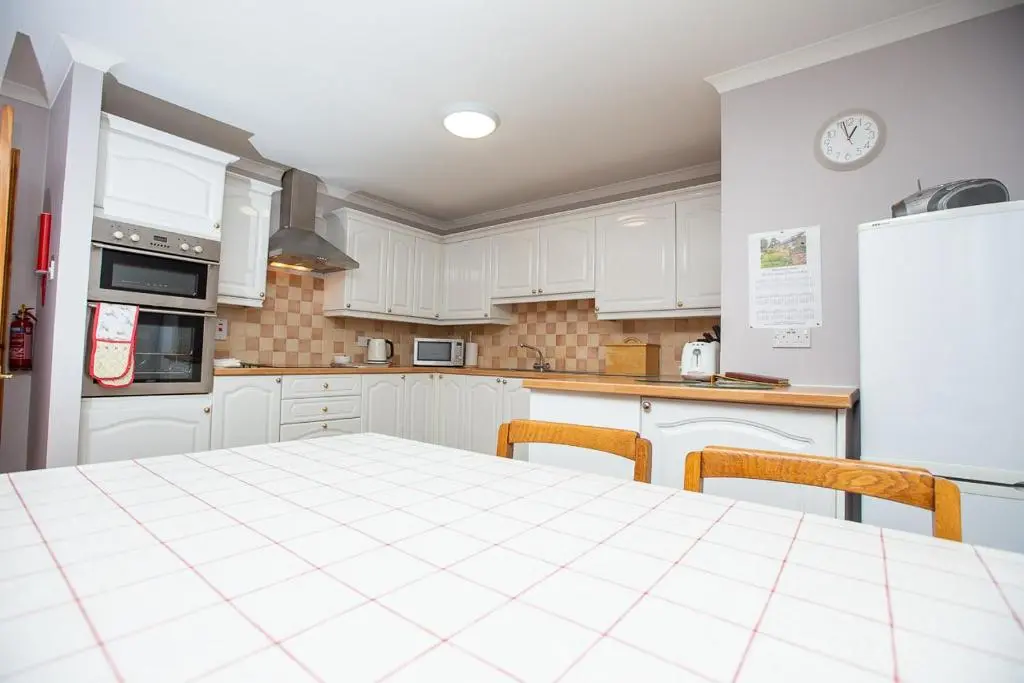 a kitchen with white cabinets and a table and a refrigerator at Ornum Cottage in Beauly